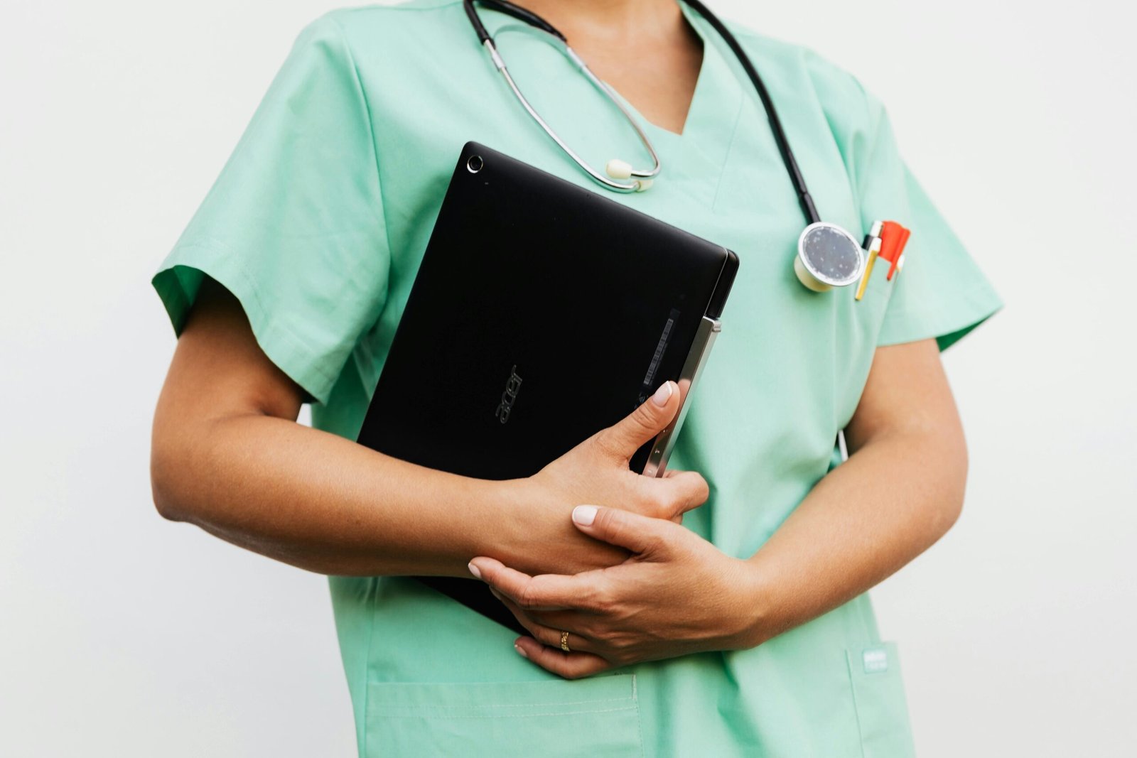 Close-up of a nurse in green scrubs holding a tablet and stethoscope, symbolizing modern healthcare.