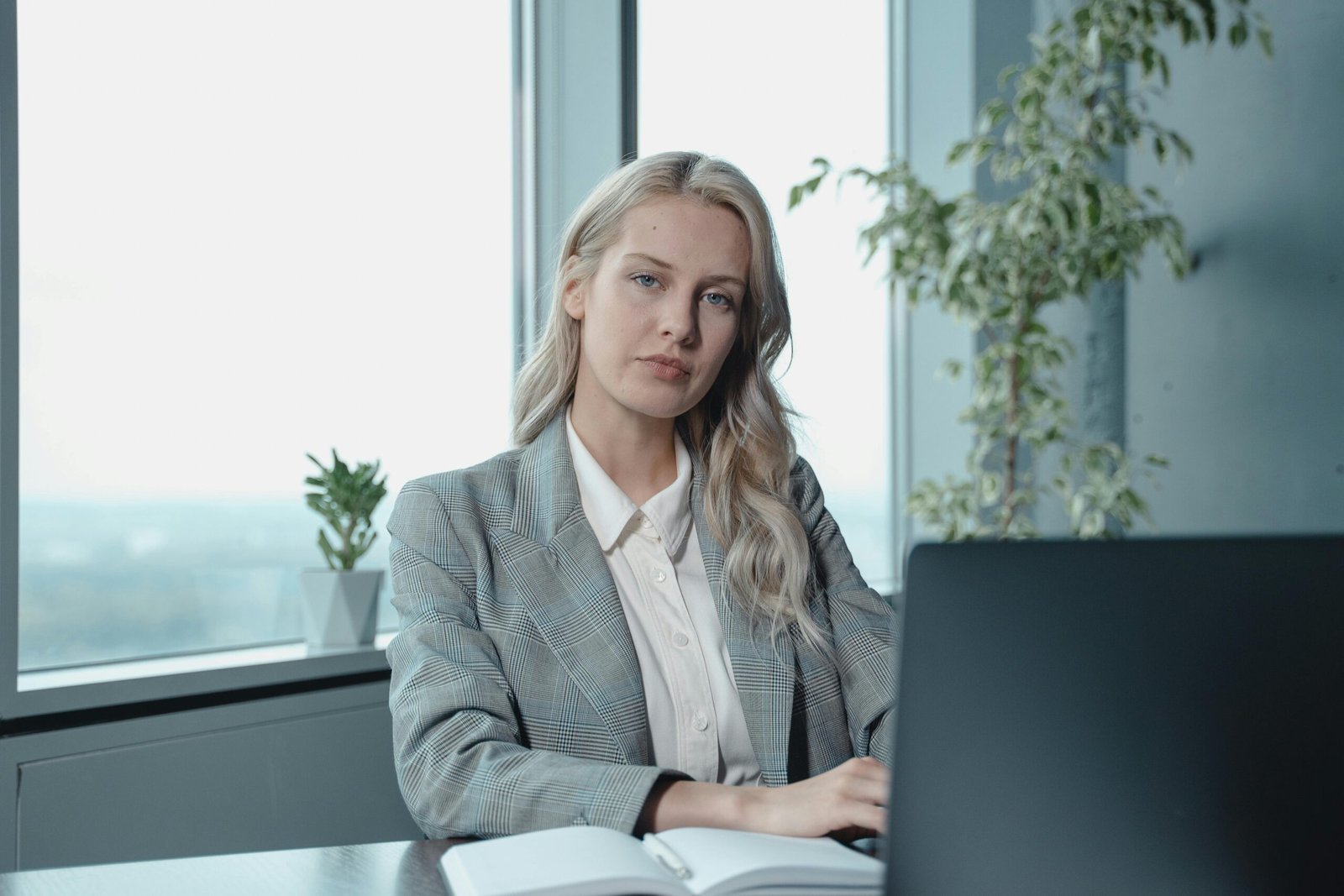 Professional businesswoman at a desk in a bright office with a laptop and notebook.