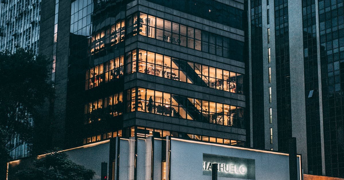 Night view of a city block with illuminated store, modern architecture, and cloudy sky.