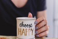 A woman holds a mug with 'choose happy' text indoors, promoting positivity.