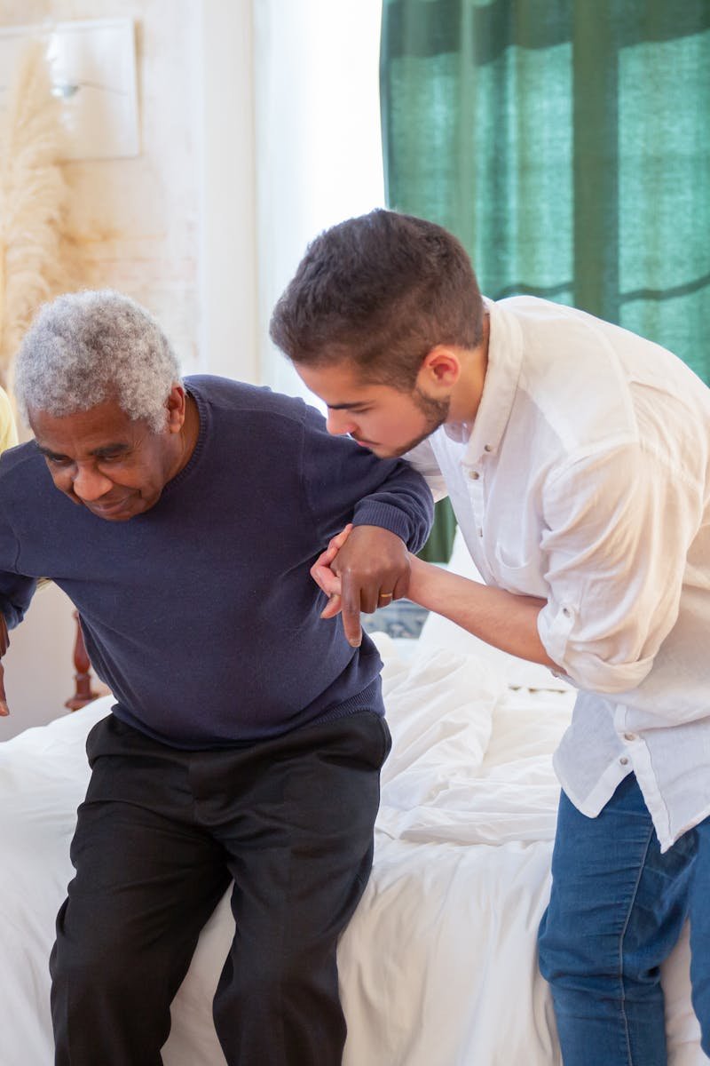 An elderly man receiving assistance from caregivers in a cozy home environment.