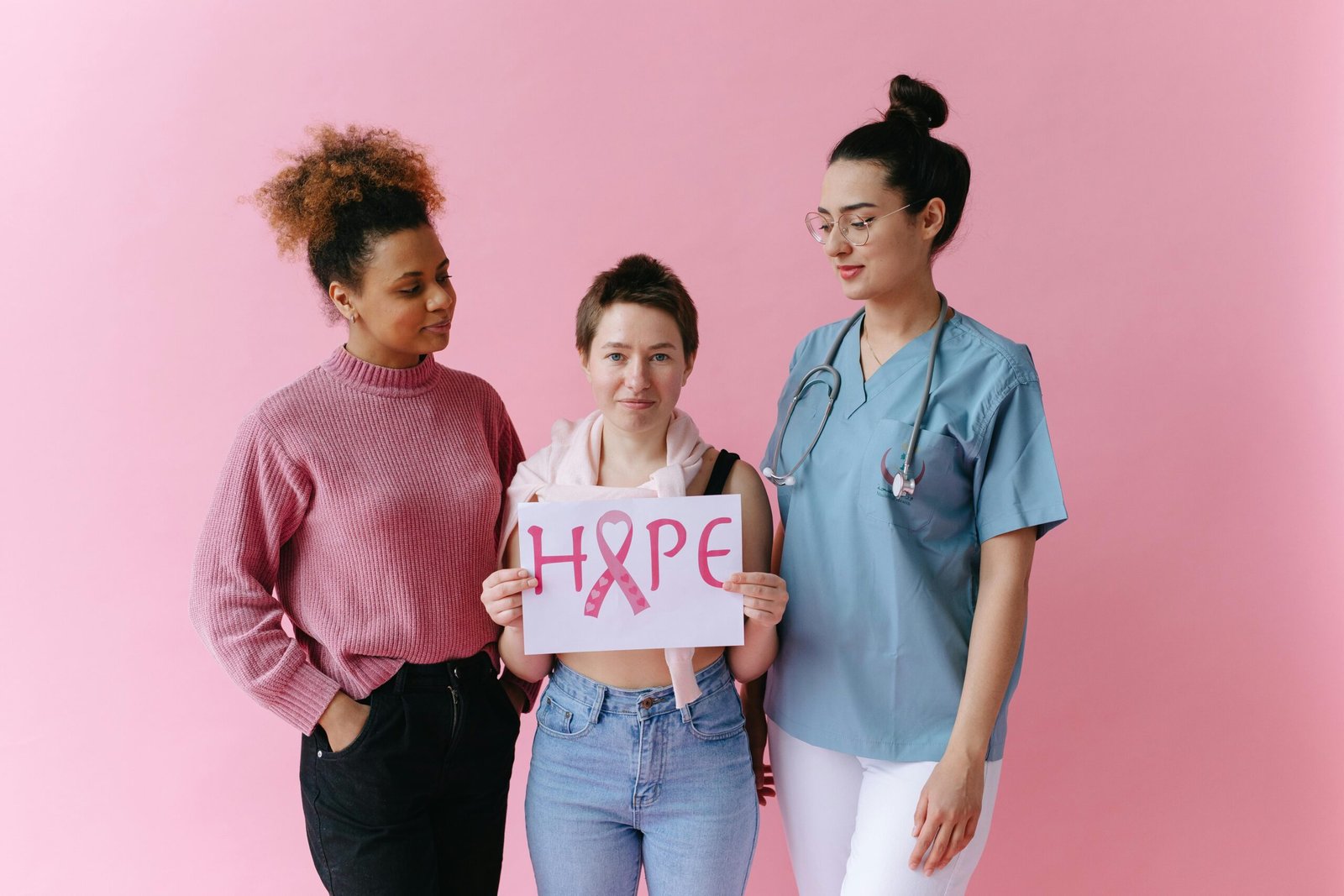 Three women supporting breast cancer awareness with a hope sign on a pink background.